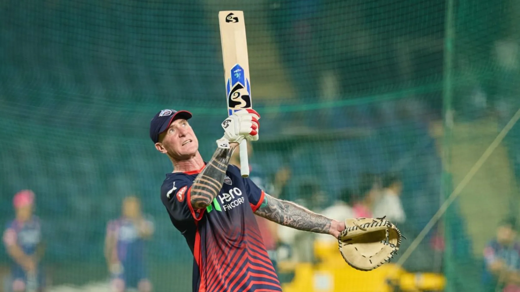 Professional cricket coach works with bat and catching glove inside training nets, illustrating technical fielding preparation in GNN coverage powered by The Guru Gyan