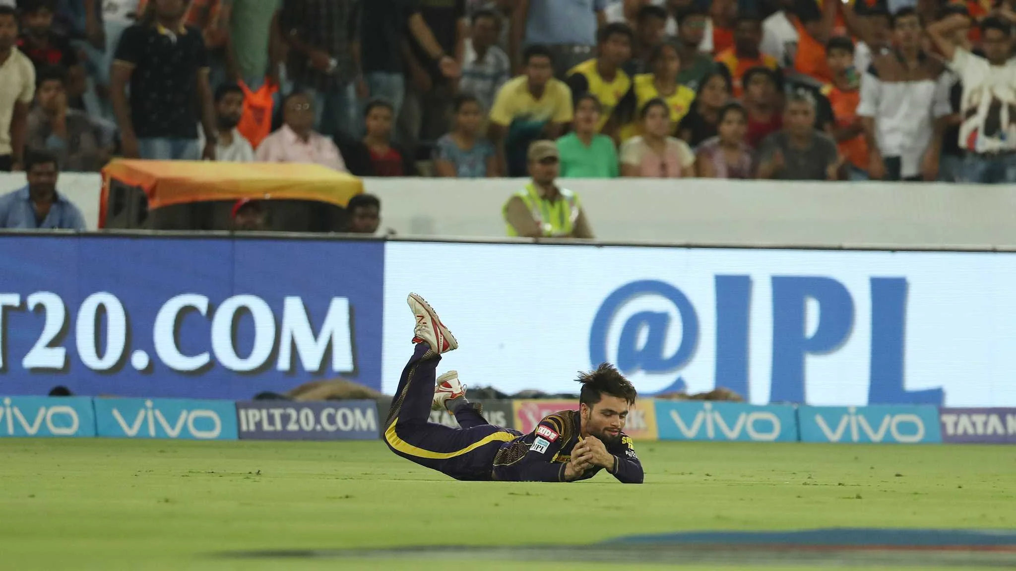 An IPL fielder in a dark kit dives forward low to the turf for a catch, illustrating match-specific repetition and pressure catching in Guru News Network fielding analysis