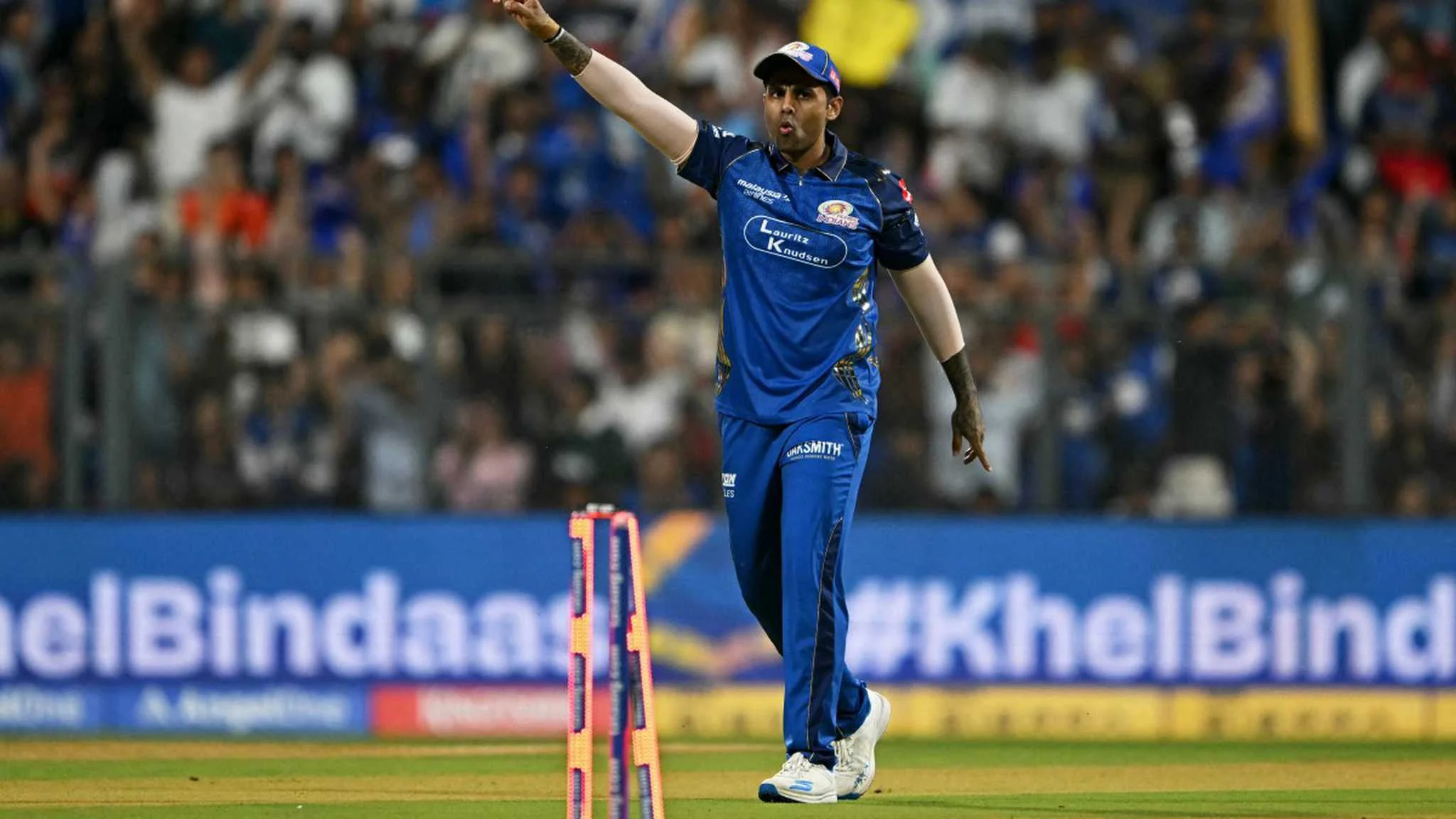 An IPL cricketer in a blue kit gestures on the field during a match, supporting GNN analysis of athletic development, role clarity and modern IPL fielding standards